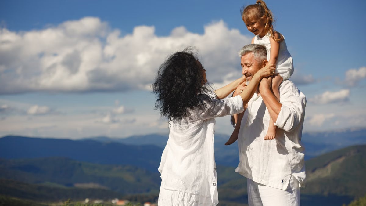 Grandparents with granddaughter having fun in nature. Scenic mountain view and joyful family moment.