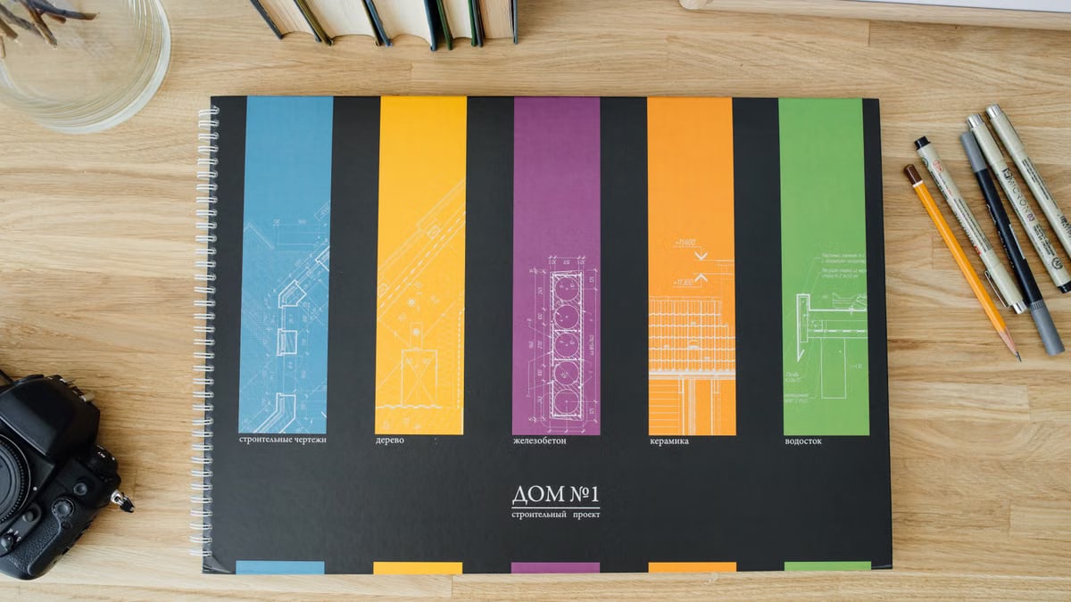 Design and architecture workbook with colorful blueprints on a wooden desk.
